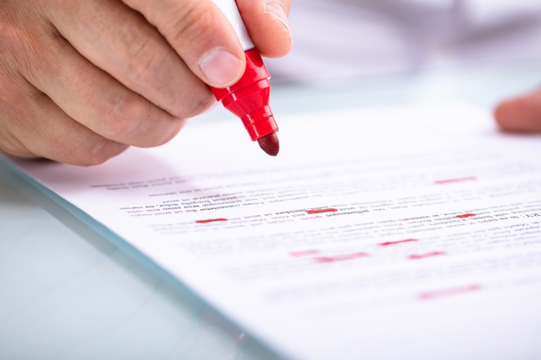 Close-up of a hand holding a red marker pen and marking a document